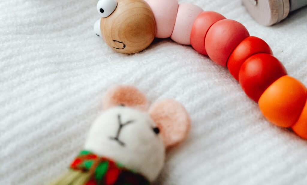 A toy worm and toy mouse lying on a white blanket.